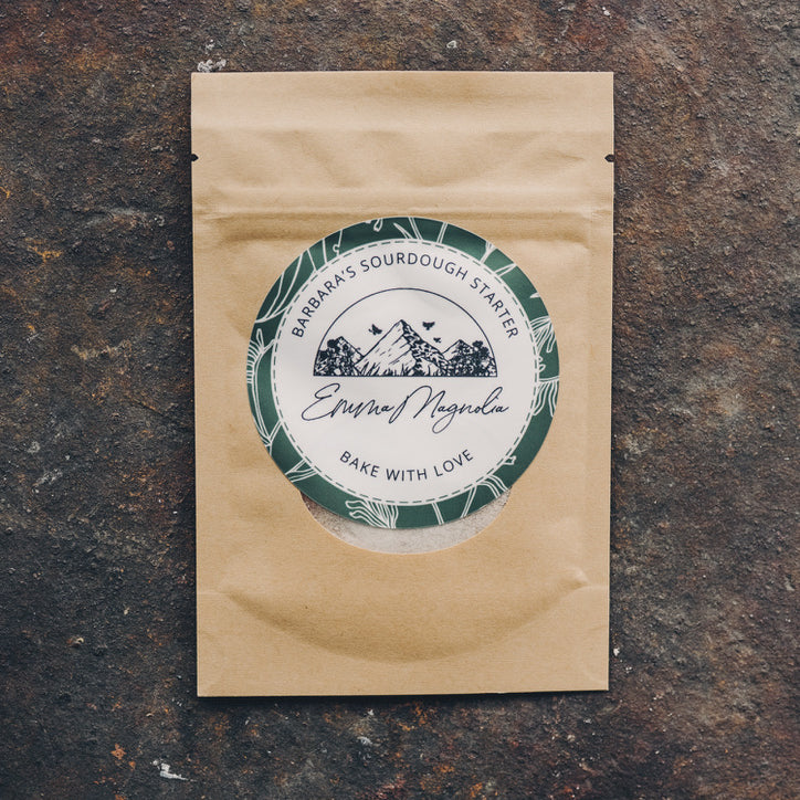 Paper tea package with a green and white label from Emma Magnolia on a dark stone surface