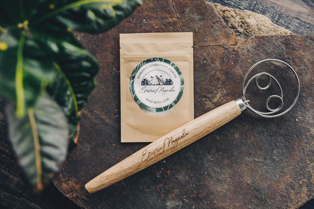 Tea package and wooden handle whisk made by Emma Magnolia on a rustic stone surface with a plant in the corner.