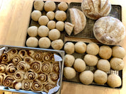 Assorted sourdough breads including rolls, buns, and cinnamon buns on a wooden surface.