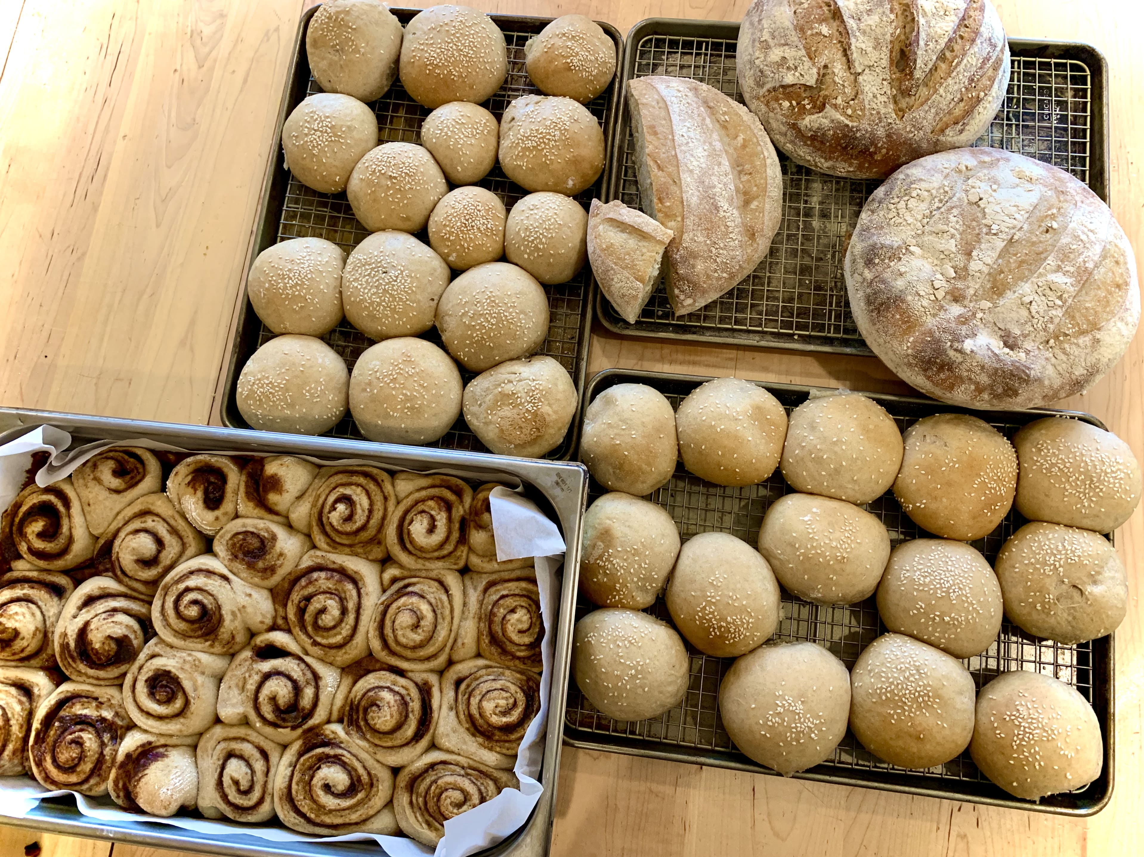 Assorted sourdough breads including rolls, buns, and cinnamon buns on a wooden surface.